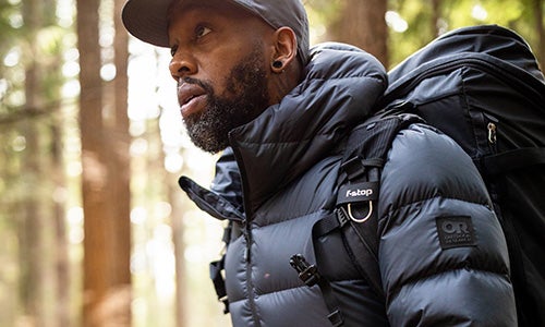 Man wearing a grey cap and a navy blue down puffy hoodie in the woods