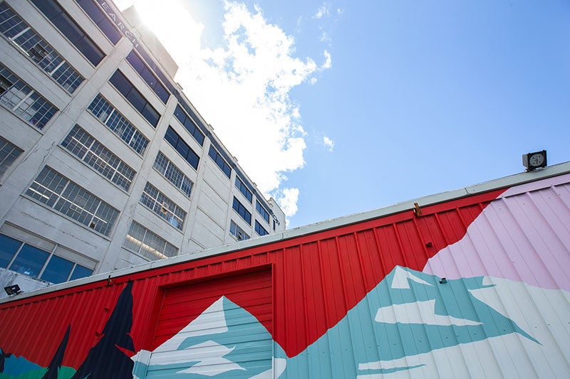 Looking up at the Outdoor Research Seattle Headquarters building, with a colorful mural in the foreground and blue skies above.