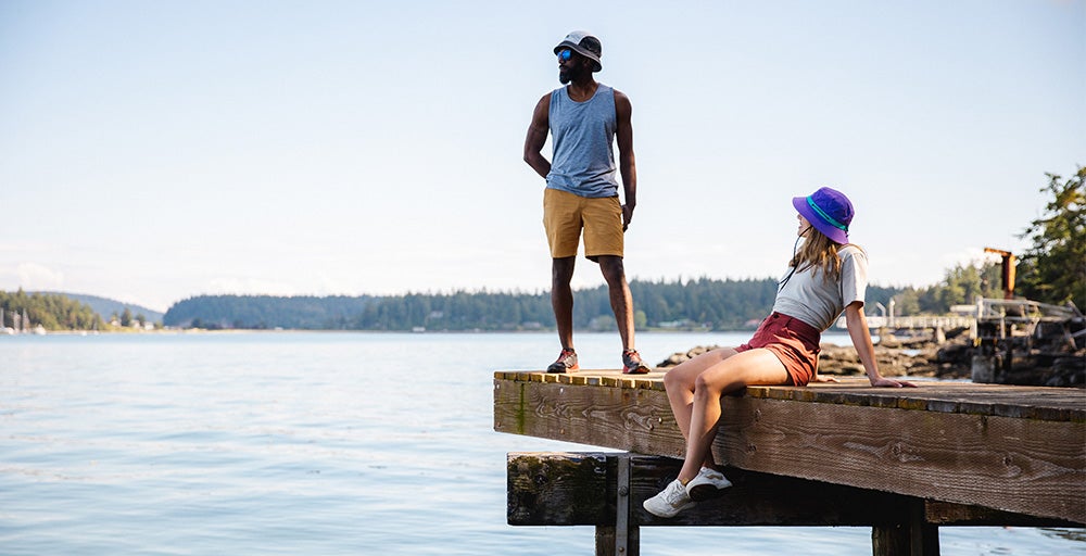 A man and a woman wearing Outdoor Research clothing sit on a dock in summer.